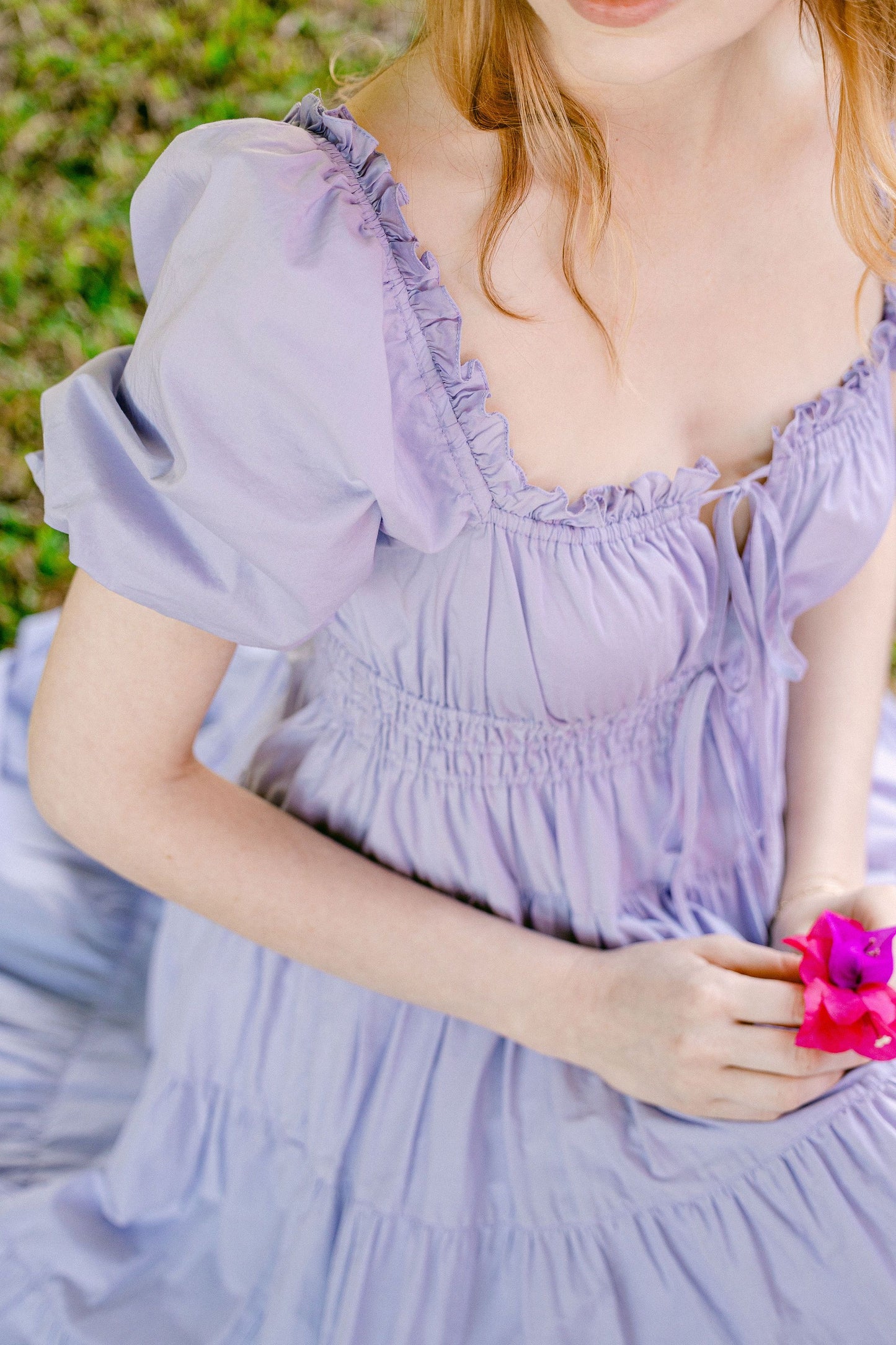 Model holds flowers and wears Penelope Dress - Lilac in secret garden