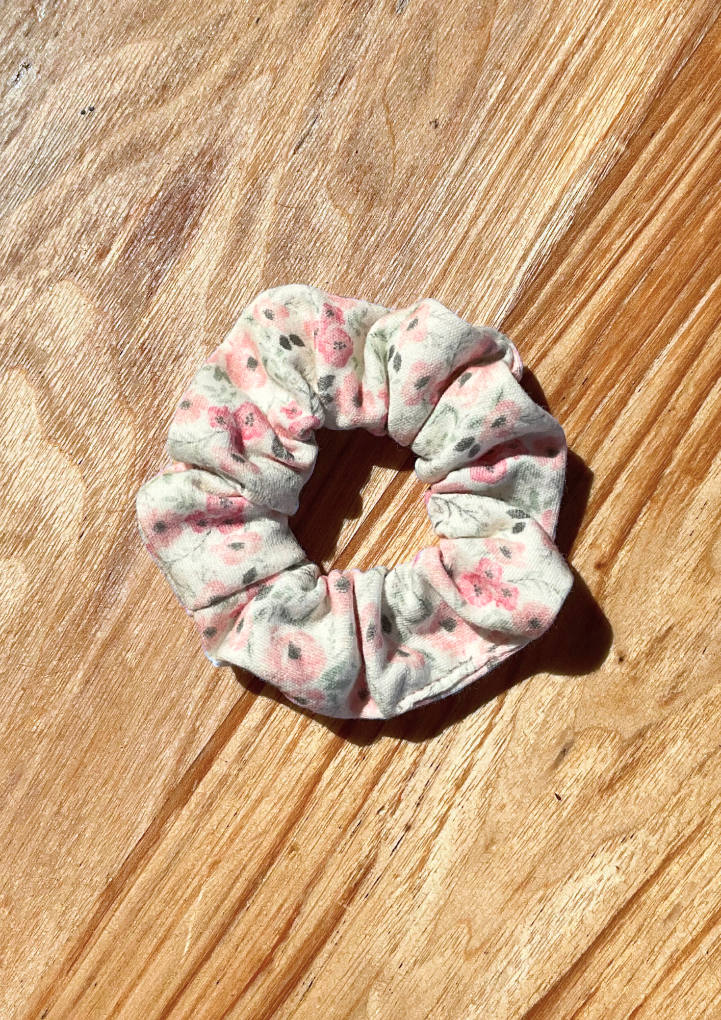 Pink Meadow Scrunchie. Floral print. White background with tiny pink and gray flowers. Eravela handmade organic cotton scrunchie with soft organic cotton elastic.