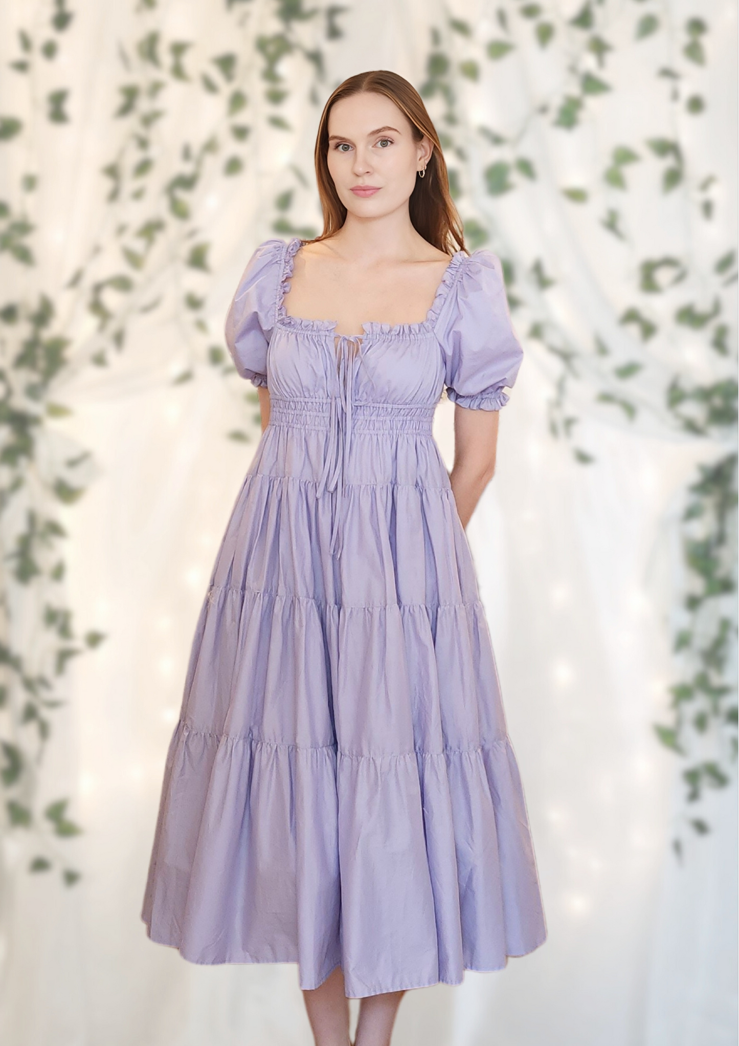 Elegant lilac midi dress with puff sleeves – the Penelope Dress by Eravela, crafted from organic cotton with a tiered skirt, adjustable bow ties, and a flattering cinched waist. Perfect for weddings, brunch, garden parties, and summer occasions. A feminine and timeless flowy dress designed for effortless elegance and comfort.